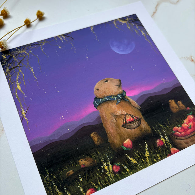 A square art print with a white border, featuring a whimsical illustration of a prairie dogs wearing a blue bow tie and holding a basket of peaches in a field under a purple night sky with a moon, displayed on a light marble surface.