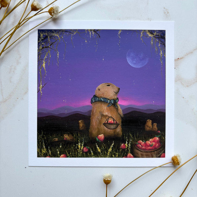 A square art print featuring a whimsical illustration of a prairie dog standing in a field at night under a purple sky with a moon, surrounded by dried flowers on a light marble surface.